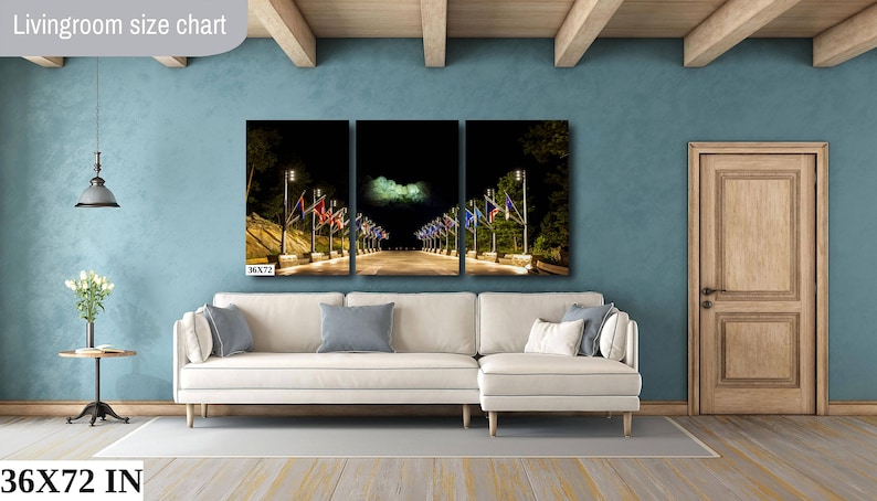 May include: A three-panel canvas print depicting a night scene of a street lined with flags and streetlights. The print is displayed on a white sectional sofa in a living room with a light blue wall and wooden beams. The text "36X72 IN" is visible in the bottom left corner of the image.