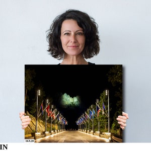 May include: A black and white photograph of Mount Rushmore at night with a row of flags lining the road leading up to the monument. The flags are lit up with string lights.