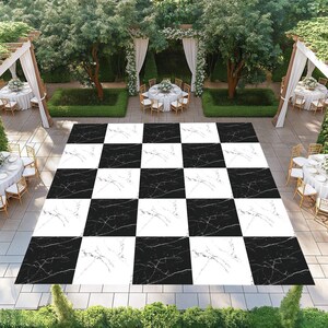 May include: A black and white checkered dance floor with a marble pattern. The outdoor setting includes tables with white tablecloths, chairs, and floral arrangements. Green hedges and trees surround the area, creating a garden-like atmosphere.