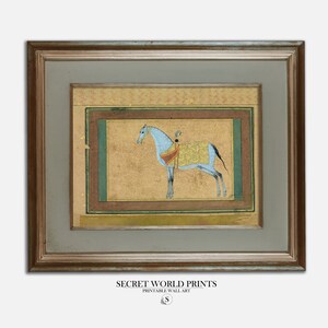 May include: A framed painting of a blue horse with a rider in a gold and red outfit. The horse is standing on a gold background with a green border. The painting is framed in a gold frame.
