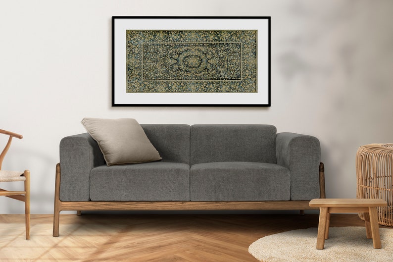 K&ouml;nnte beinhalten: Ein graues Stoff-Sofa mit einem Holzrahmen und einem beigefarbenen Kissen. &Uuml;ber dem Sofa h&auml;ngt ein gerahmtes Bild eines blauen und goldenen gemusterten Teppichs.