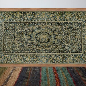 K&ouml;nnte beinhalten: Ein gerahmter Vintage-Teppich mit dunkelblauem Hintergrund und aufwendigen goldenen Blumenmustern. Der Teppich befindet sich in einem Holzrahmen.
