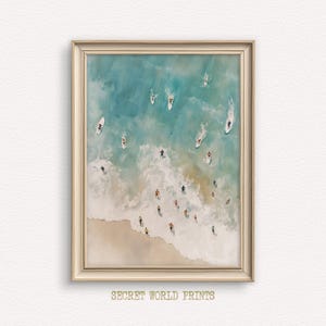 Op de afbeelding: Een ingelijste prent die een strandscène met surfers in de oceaan weergeeft. Het kunstwerk toont een zandstrand, schuimende golven en turquoise water. Surfers rijden op witte surfplanken. De tekst "SECRET WORLD PRINTS" staat onderaan het frame.