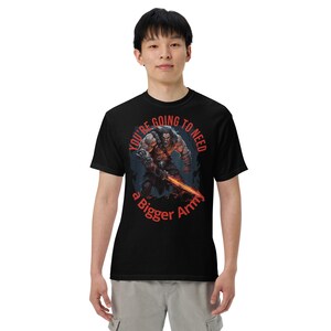 Op de afbeelding: Zwart T-shirt met een rode afbeelding van een gespierde man die een zwaard vasthoudt. De afbeelding is omgeven door een cirkel met de tekst "You're going to need a bigger army".