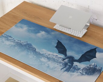 May include: A rectangular desk mat featuring a fantasy scene with a dragon soaring over snow-capped mountains under a cloudy sky. The dragon is dark blue, and the mountains are white. A laptop and keyboard are on the desk.