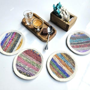 May include: Four colorful round coasters with a white border. The coasters are made of woven fabric with a variety of colors and patterns.