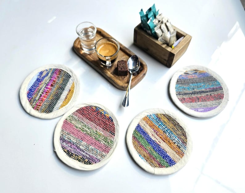 May include: Four colorful round coasters with a white border. The coasters are made of woven fabric with a variety of colors and patterns.