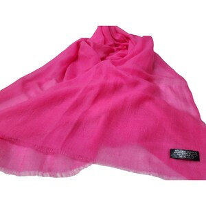 Puede incluir: Una bufanda de cachemira rosa brillante con un borde de flecos. La bufanda tiene una etiqueta negra con el texto "Exclusive Cashmere Hand Made in Nepal 100% Cashmere Dry Clean Only".