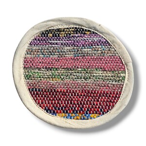 May include: Round woven rug with a white border and a colorful striped pattern in shades of pink, red, green, blue, and purple.