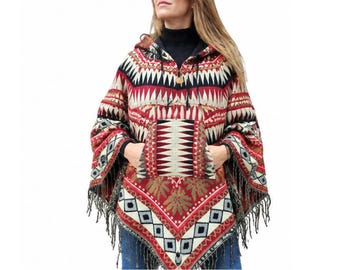 May include: A hooded poncho featuring a vibrant geometric pattern in red, black, white, and tan. The garment includes a large front kangaroo pocket, a drawstring hood, and a hemline finished with long, dark fringe detailing along the edges.