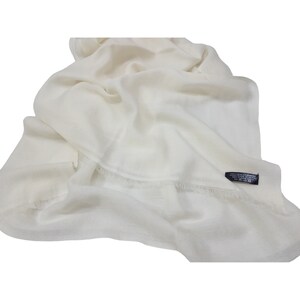 Puede incluir: Una bufanda de pashmina blanca con borde de flecos. La bufanda está hecha de 100% cachemira y está tejida a mano en Nepal. La etiqueta en la bufanda dice "Exclusive Cashmere 100% Pure Cashmere Hand Made in Nepal."