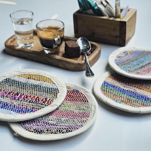 May include: Four colorful woven coasters with a white border. The coasters are made of recycled materials and are perfect for protecting surfaces from heat and spills.