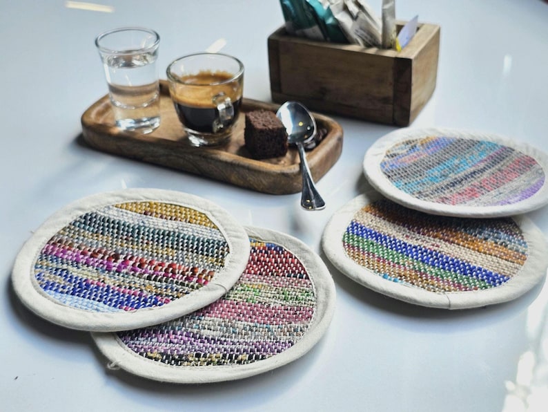 May include: Four colorful woven coasters with a white border. The coasters are made of recycled materials and are perfect for protecting surfaces from heat and spills.