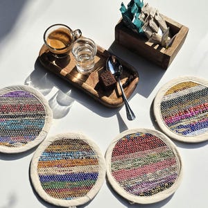 May include: Four colorful woven coasters with a white border. The coasters are made of recycled materials and have a unique, handmade look.