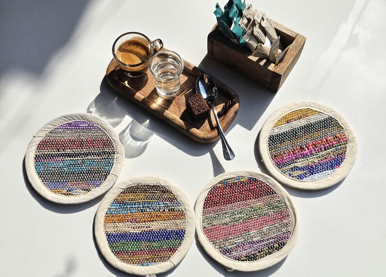 May include: Four colorful woven coasters with a white border. The coasters are made of recycled materials and have a unique, handmade look.