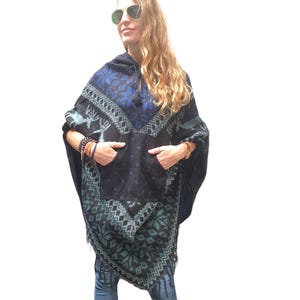 May include: A blue and black hooded poncho with a geometric pattern and fringe. The poncho has two pockets and a deer design.