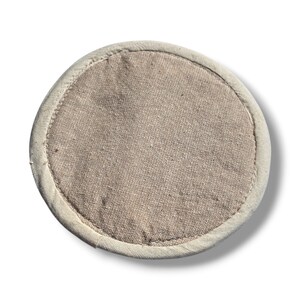 May include: A round, beige-colored, fabric coaster with a white border.
