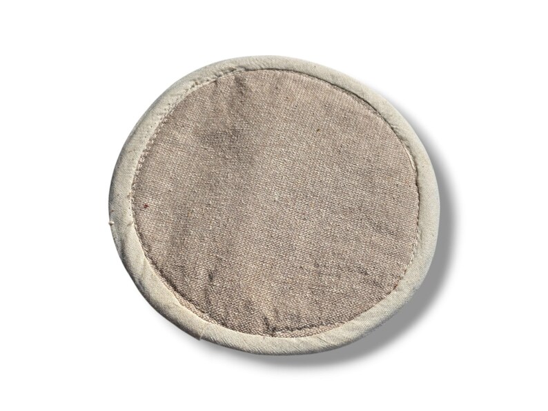 May include: A round, beige-colored, fabric coaster with a white border.
