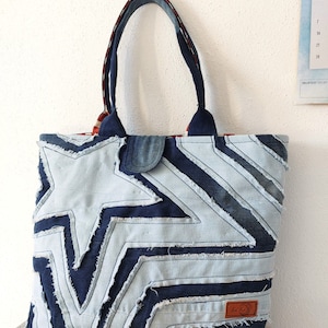 Könnte beinhalten: Eine blaue Jeans-Tragetasche mit Sternenmuster. Die Tasche hat zwei Henkel und ein braunes Leder-Etikett mit dem Wort "Love" darauf.