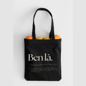 May include: Black canvas tote bag with the text "Ben l&agrave;." and a definition in French. The bag is filled with oranges.
