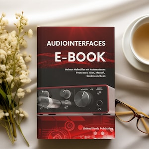 Puede incluir: Un libro rojo y negro titulado "Audiointerfaces E-Book" con el nombre del autor y una foto de una pequeña interfaz de audio en la portada. El libro está sobre una superficie blanca con una taza de té y unas gafas.