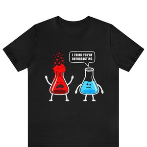 Puede incluir: Camiseta negra con un gráfico de dos vasos de precipitados, uno rojo y otro azul. El vaso rojo está explotando y tiene una expresión de sorpresa. El vaso azul tiene una expresión triste y un globo de diálogo que dice "Creo que estás exagerando".