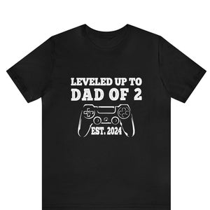 Op de afbeelding: Zwart T-shirt met witte tekst die "LEVELED UP TO DAD OF 2 EST. 2024" luidt en een witte afbeelding van een videogamecontroller.