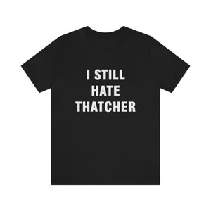 Puede incluir: Camiseta negra con texto blanco que dice "I still hate Thatcher".