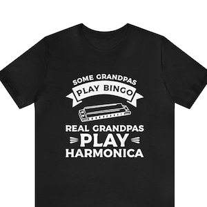 Puede incluir: Camiseta negra con texto blanco que dice "Some Grandpas Play Bingo. Real Grandpas Play Harmonica."  Se muestra una armónica sobre el texto.