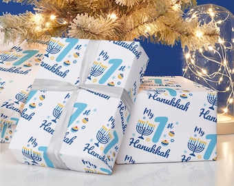 May include: White gift wrap with a blue and yellow repeating pattern of a menorah, the number one, the words "My 1st Hanukkah", and a blue and yellow donut.