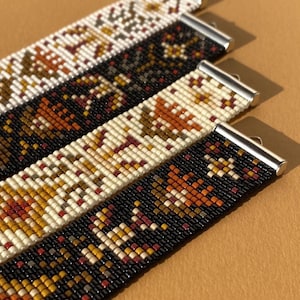 May include: Four beaded bracelets with silver clasps. The bracelets feature intricate patterns in black, white, brown, orange, and burgundy. The bracelets are displayed on a brown surface, showcasing the detailed beadwork and color combinations.
