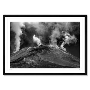 May include: A black and white photograph of a volcano with smoke billowing from the top. The volcano is covered in ash and the sky is cloudy.