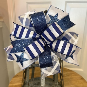 May include: A blue and white striped ribbon bow with silver glitter and star accents. The bow is tied around a metal container.
