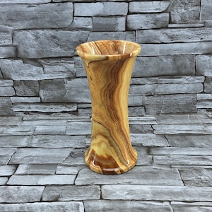 May include: A wooden vase with a natural wood grain pattern. The vase is light brown with streaks of darker brown and has a flared opening.