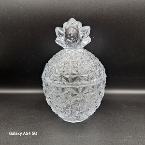 Könnte beinhalten: Ein klares Glasgefäß in Form einer Ananas mit einer strukturierten Oberfläche. Das Gefäß hat einen Deckel mit einem Ananas-Design.