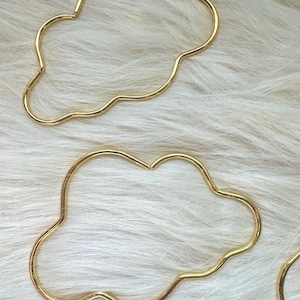 May include: Two gold cloud-shaped hoops. The hoops are made of a thin metal and have a smooth, polished finish.