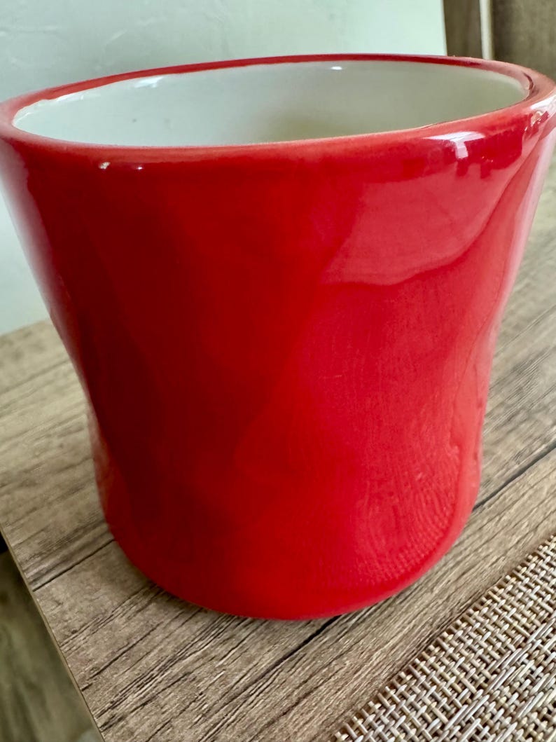 May include: A bright red ceramic plant pot with a glossy finish. The pot has a wide opening and a gently curved shape, with a white interior. Suitable for indoor or outdoor use, it is a decorative item.