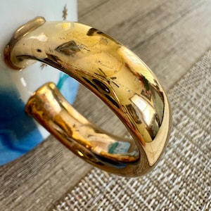 May include: A ceramic mug handle with a reflective gold metallic finish. The mug body features a white surface decorated with small gold star patterns and a blue gradient design visible near the base of the handle attachment points.