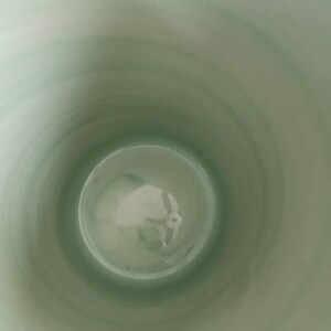 May include: A light green ceramic vase interior, viewed from above. The inside of the vase has a smooth, glossy finish. The color transitions from a lighter green at the top to a darker shade towards the bottom. The vase appears to be empty.