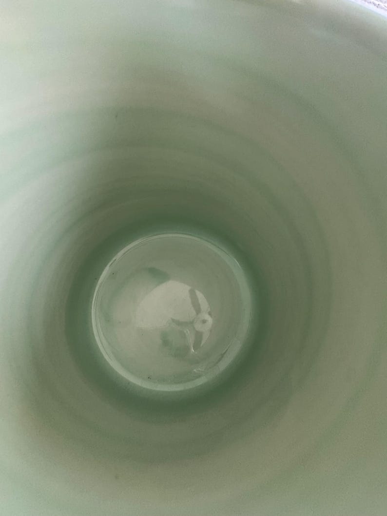 May include: A light green ceramic vase interior, viewed from above. The inside of the vase has a smooth, glossy finish. The color transitions from a lighter green at the top to a darker shade towards the bottom. The vase appears to be empty.