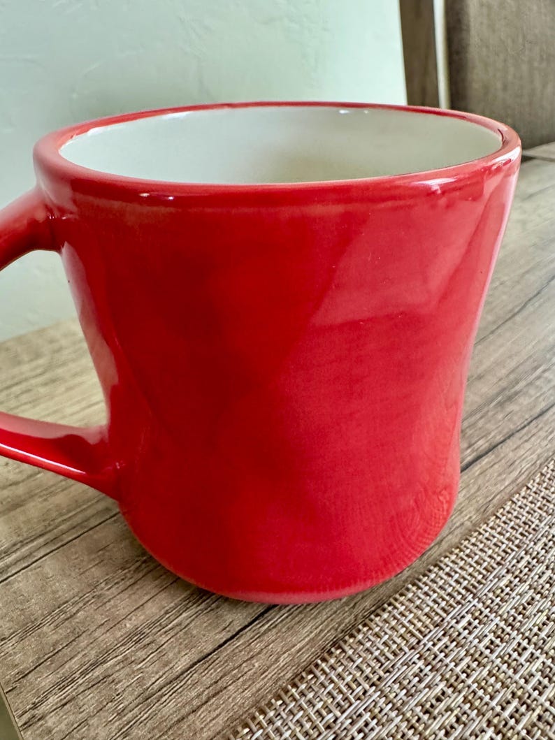 May include: A vibrant red ceramic mug with a white interior. The mug has a curved shape and a sturdy handle. The glossy finish reflects light, highlighting the smooth surface. This mug is perfect for enjoying your favorite hot beverages.