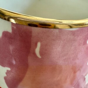 May include: A ceramic vase with a gold rim and a floral design. The vase has a cream-coloured interior and a painted exterior with shades of pink, red, and white. The gold rim adds a touch of elegance to the design.