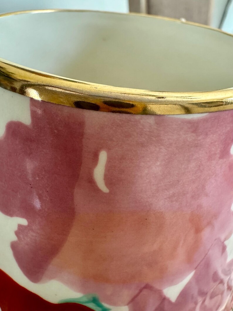 May include: A ceramic vase with a gold rim and a floral design. The vase has a cream-coloured interior and a painted exterior with shades of pink, red, and white. The gold rim adds a touch of elegance to the design.