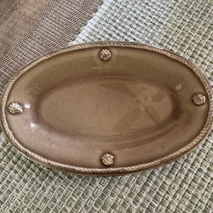 Peut inclure: Un plat ovale en céramique avec une finition brillante brun clair. Le bord présente une texture en relief rappelant une corde et quatre petits accents circulaires décoratifs et texturés placés symétriquement autour du bassin.