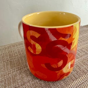 May include: A white ceramic mug with a black handle and the text "But First, Coffee" in a black, bold font. The mug is on a white surface. The mug is 4 inches tall.