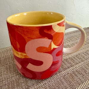 May include: A set of three ceramic mugs with a speckled, matte finish. The mugs are in shades of cream, light gray, and dark gray. Each mug has a simple, minimalist design and a rounded handle.