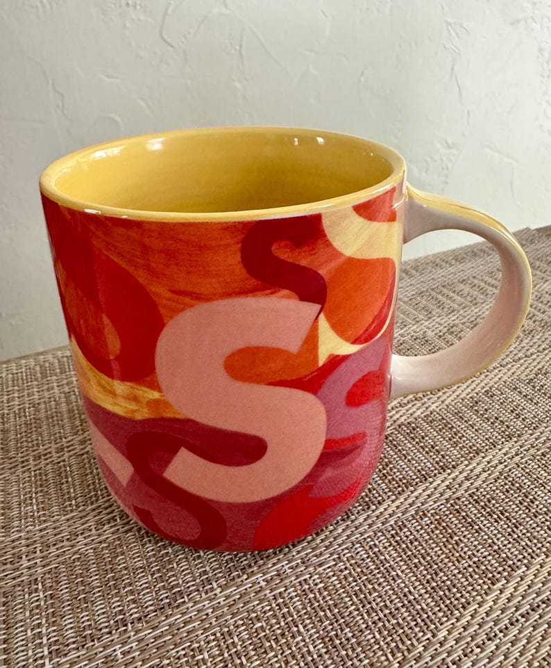 May include: A set of three ceramic mugs with a speckled, matte finish. The mugs are in shades of cream, light gray, and dark gray. Each mug has a simple, minimalist design and a rounded handle.