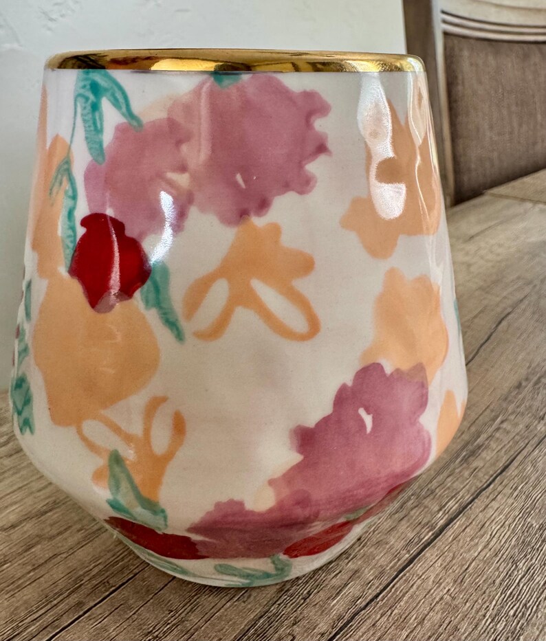 May include: A white ceramic vase with a gold rim, decorated with watercolour floral patterns in pink, orange, and red. The vase has a gently curved shape and is suitable for displaying flowers or as a decorative piece.