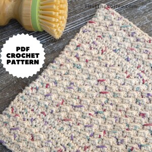 May include: A close-up of a crocheted dishcloth with a beige background and colorful flecks of yarn in pink, purple, and blue. The dishcloth is made with a simple stitch pattern and has a slightly textured surface. The text "PDF CROCHET PATTERN" is visible in the image.