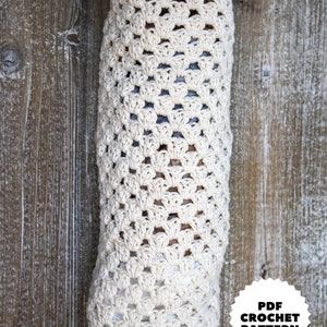 May include: A crocheted bag for storing plastic bags, hanging on a wooden wall. The bag is made with a white yarn and has a simple, open-stitch pattern. The text "PDF CROCHET PATTERN" is on a black circle with white stars.